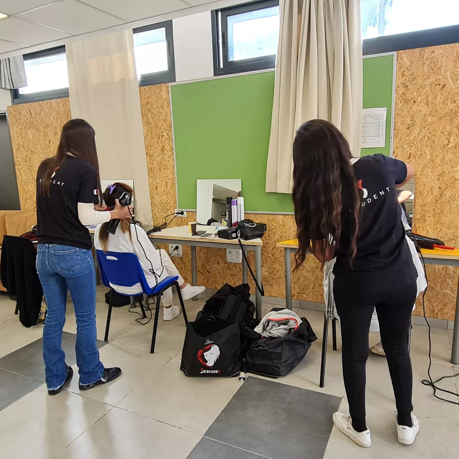 שתי תלמידות עוסקות בלימודים מעשיים בבית ספר לספרות, אחת בסגנון תספורת.