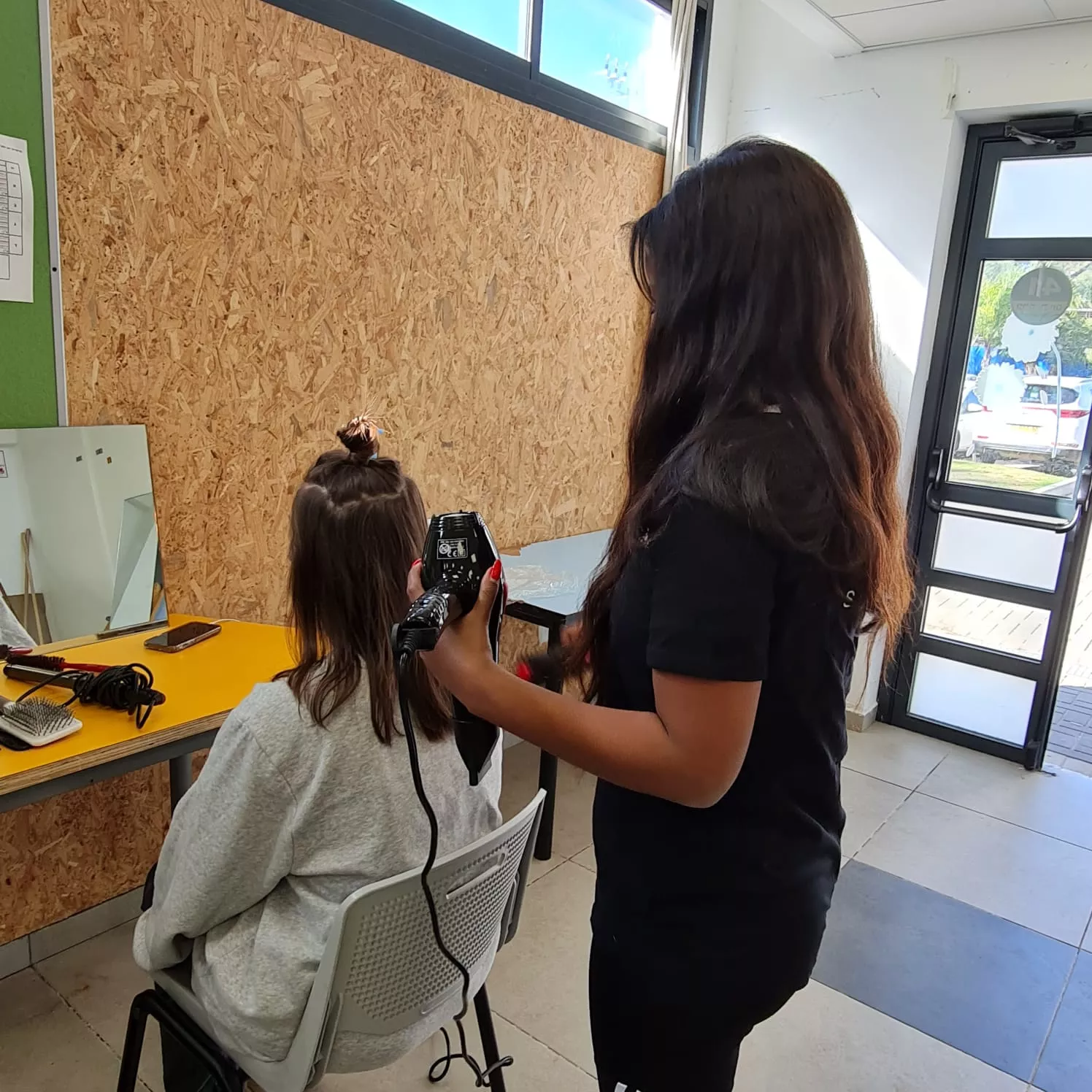 סטודנטית בלימודי עיצוב שיער מקבלת החלקות שיער במספרה מקצועית.
