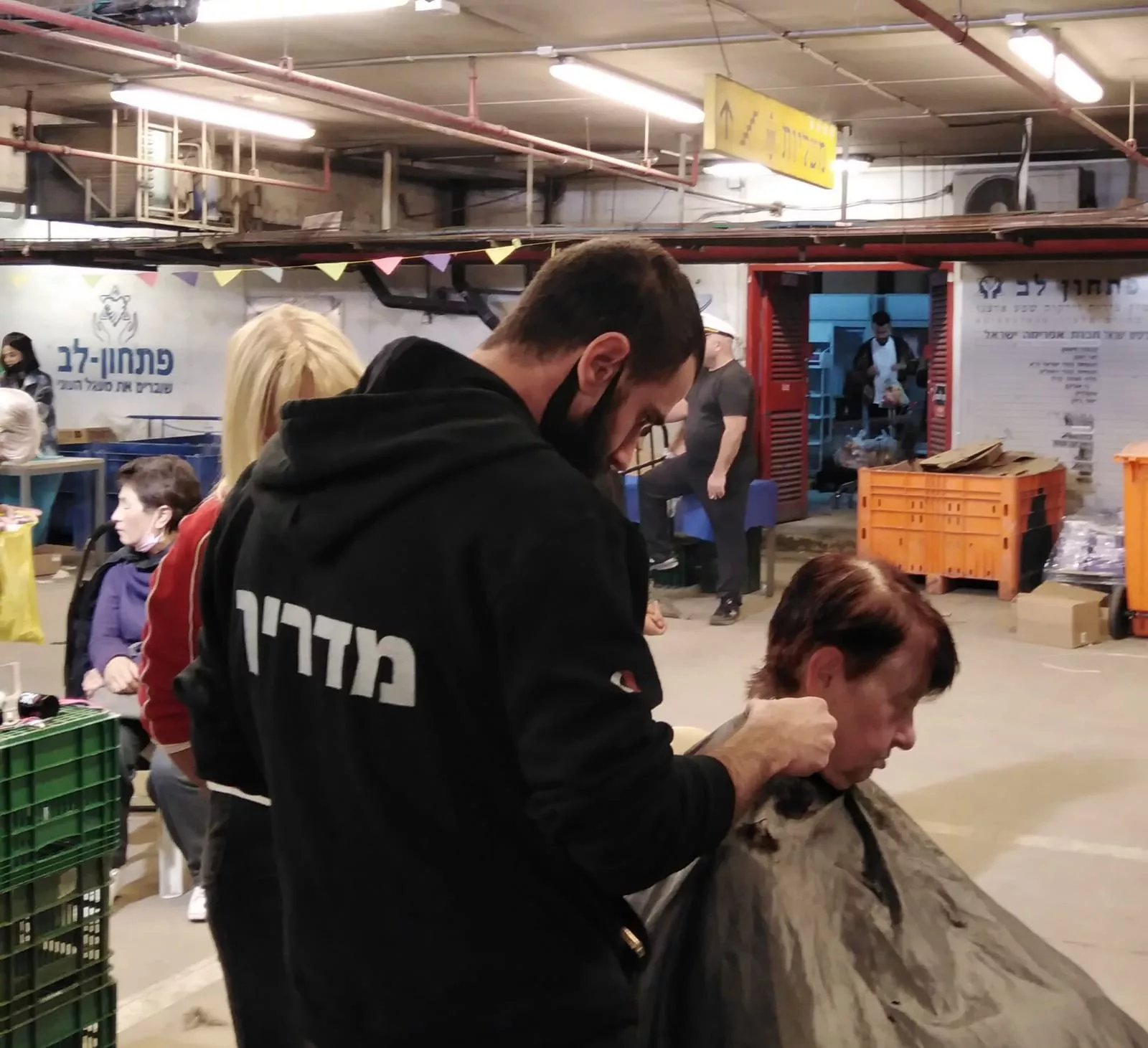ספר חותך שיער ללקוחה במרכז קהילתי, עם אנשים נוספים ברקע.