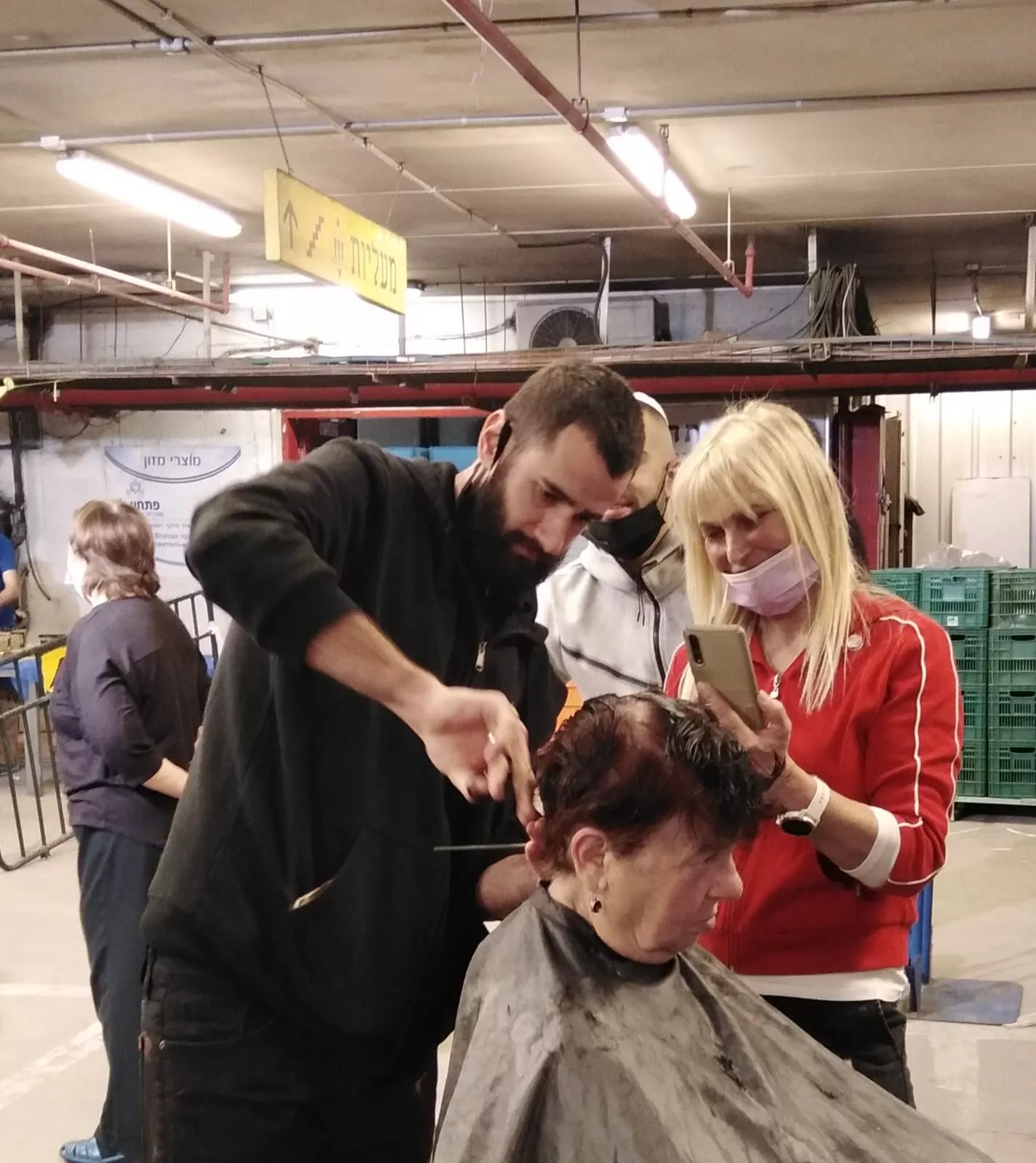 ספר חותך שיער לאישה בזמן קורס תספורות, אישה נוספת מתעדת את התהליך בטלפון.