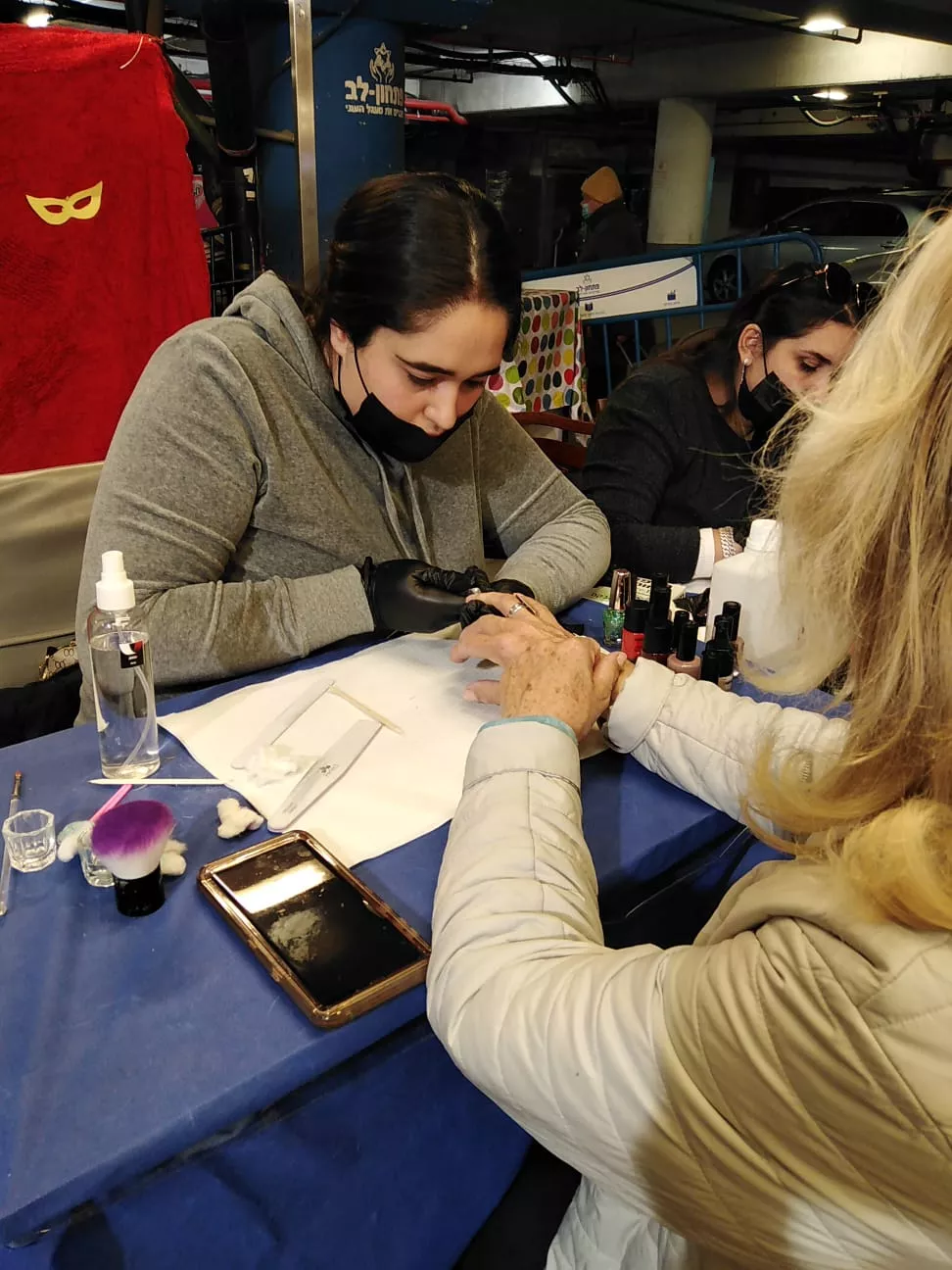 סטודנטית בקורס מניקור פדיקור מבצעת טיפול לקוחה עם לק ג'ל במרכז לימודים.