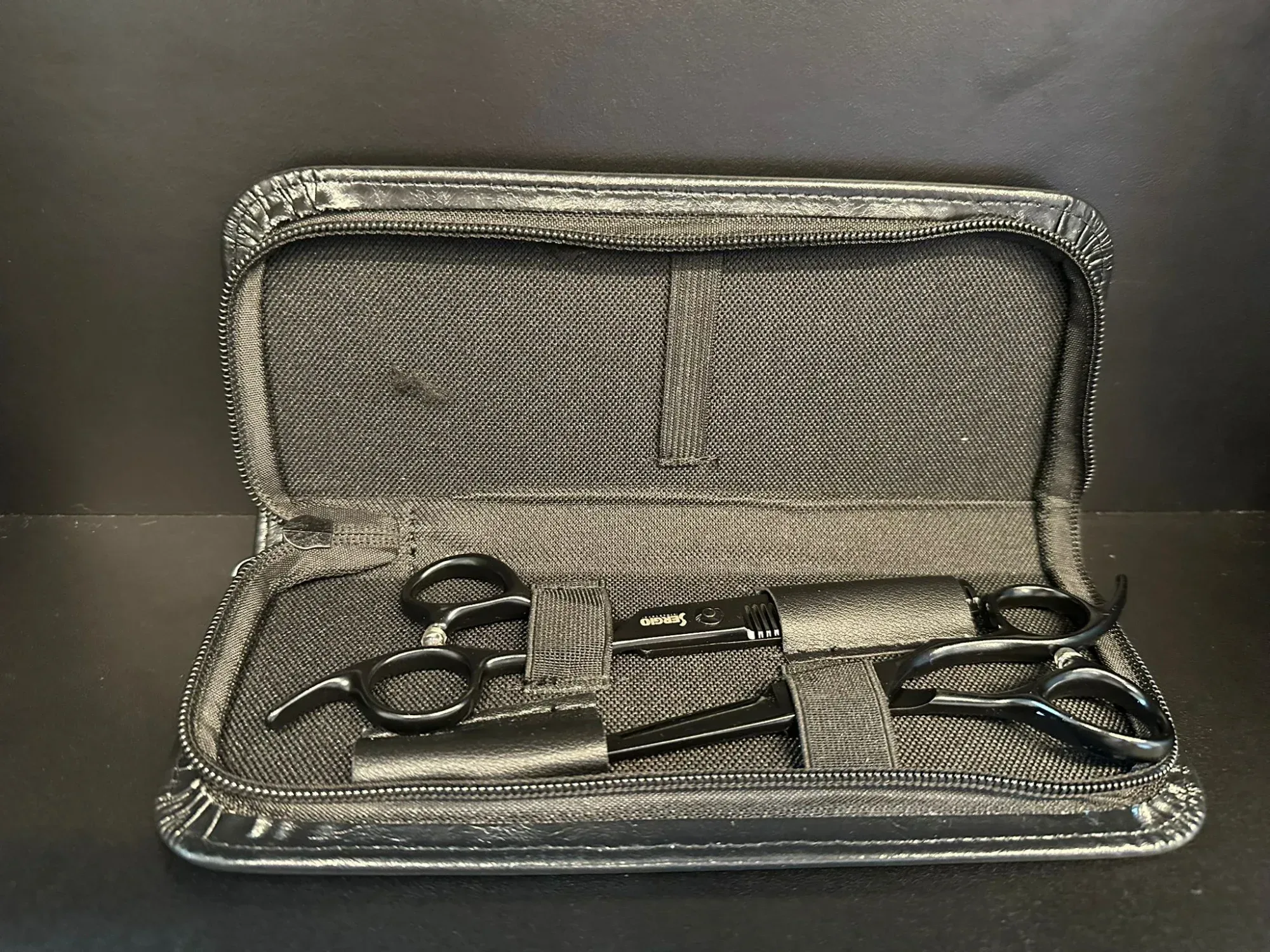 סט מספריים מקצועיים למספרות בתוך תיק שחור, מתאים לשימוש בעיצוב שיער.